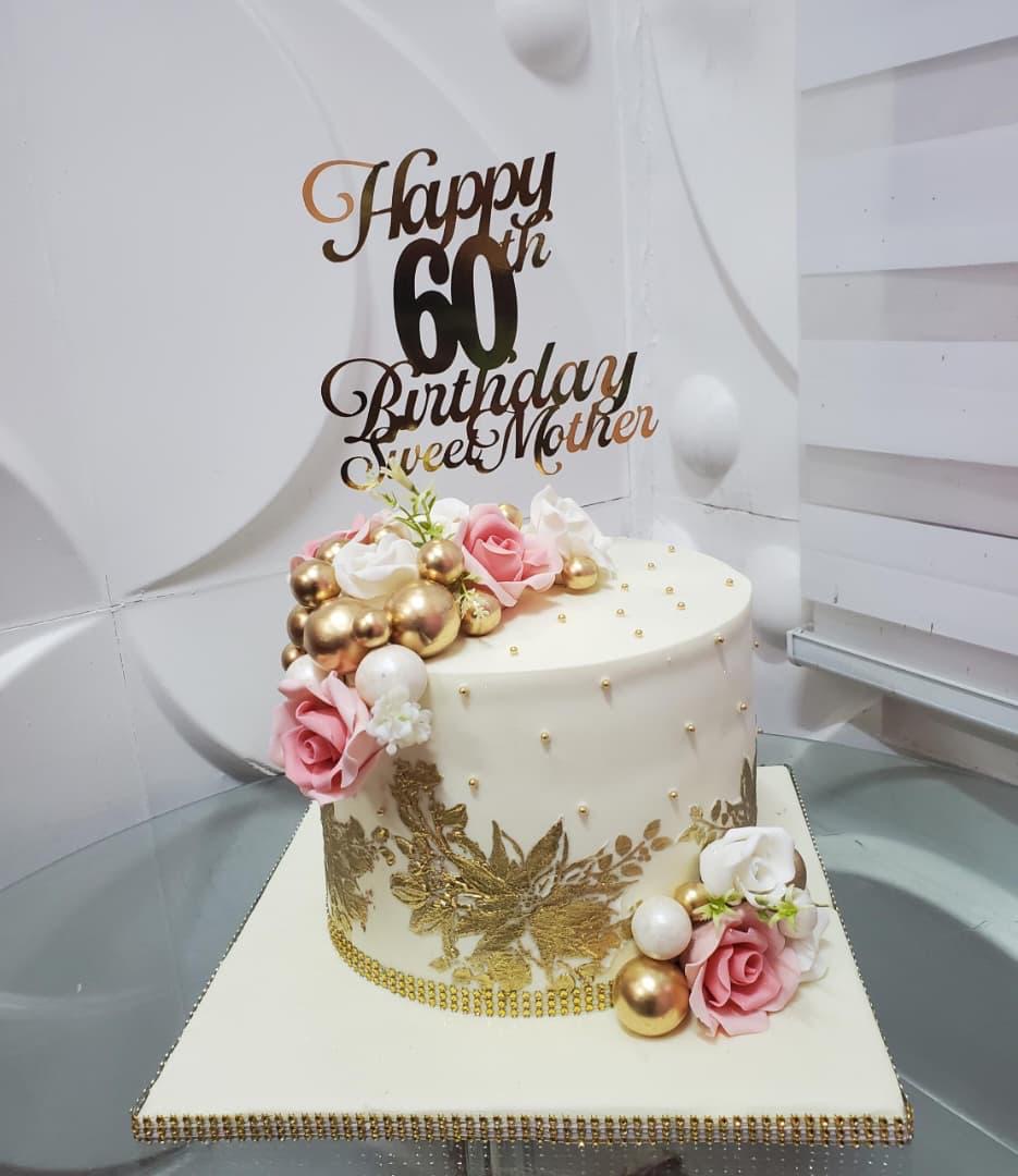 White cake decorated with gold details and pink-and-white flowers.