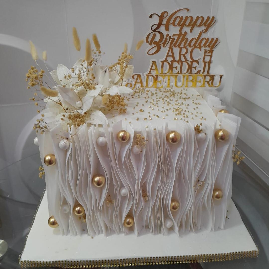 Rectangular white cake with textured icing and gold accents.