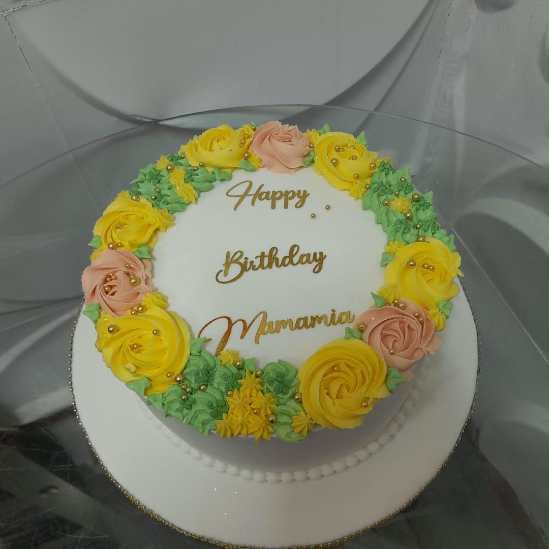 Round white cake topped with colorful piped flowers and a birthday message.