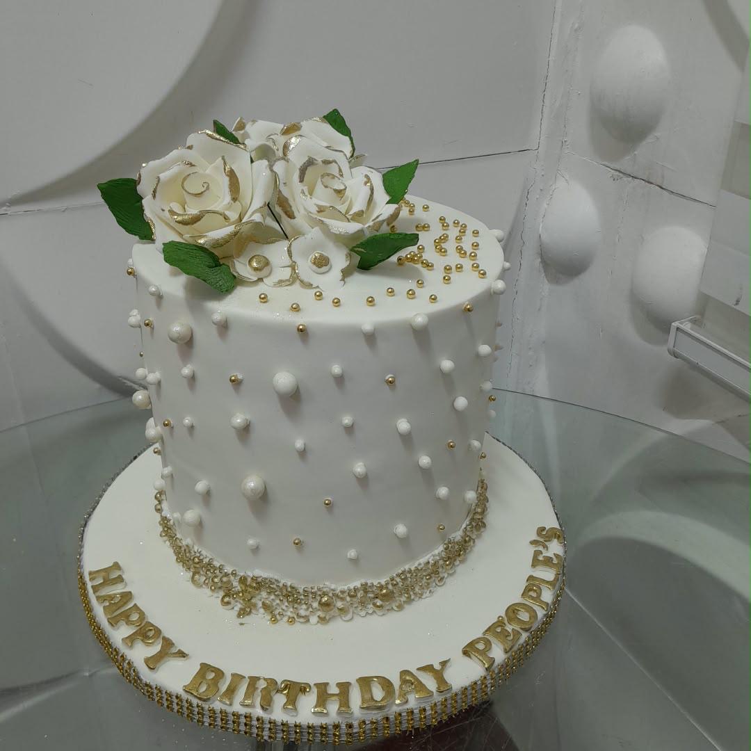 Tiered white cake decorated with piped pearls, white flowers, and gold details.