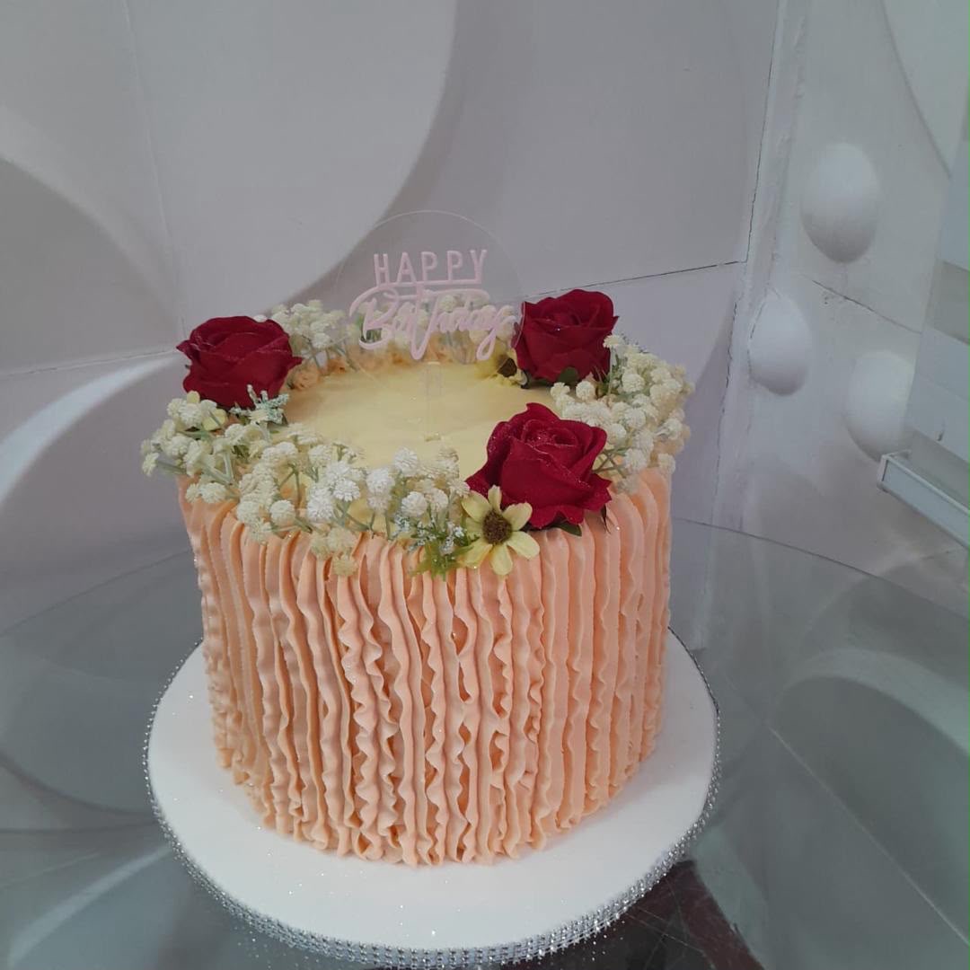 Tall peach cake with ridged icing and red flowers.