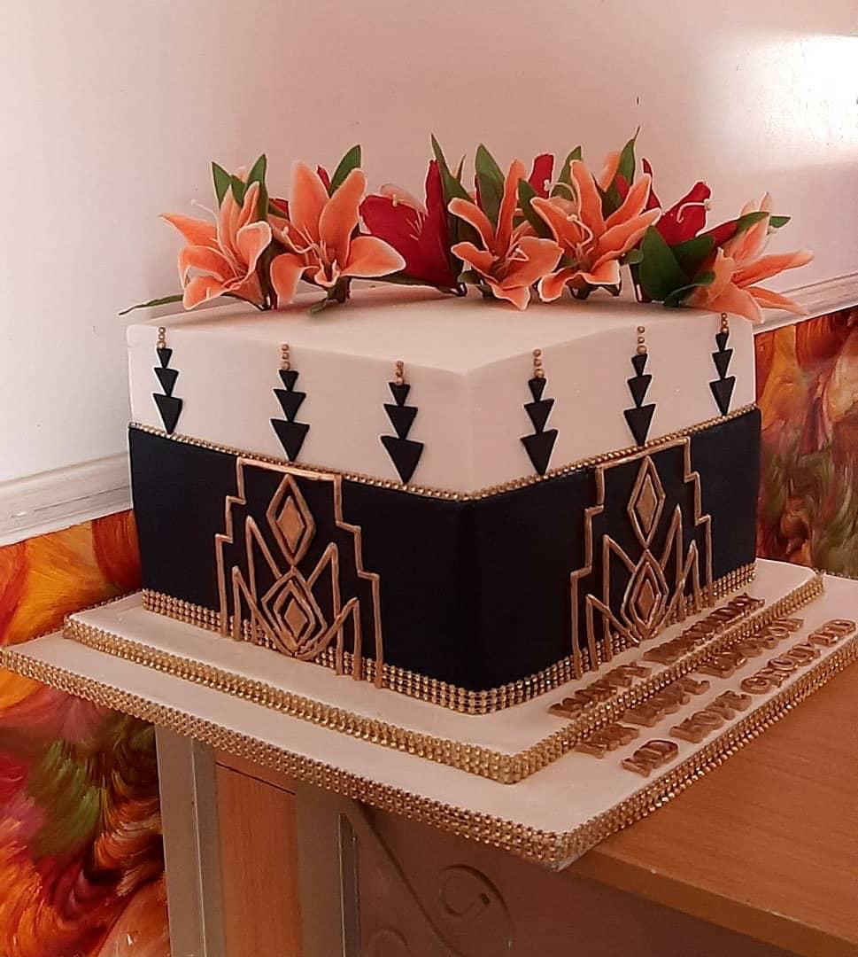 Square cake with dark geometric sides and orange flowers on top.
