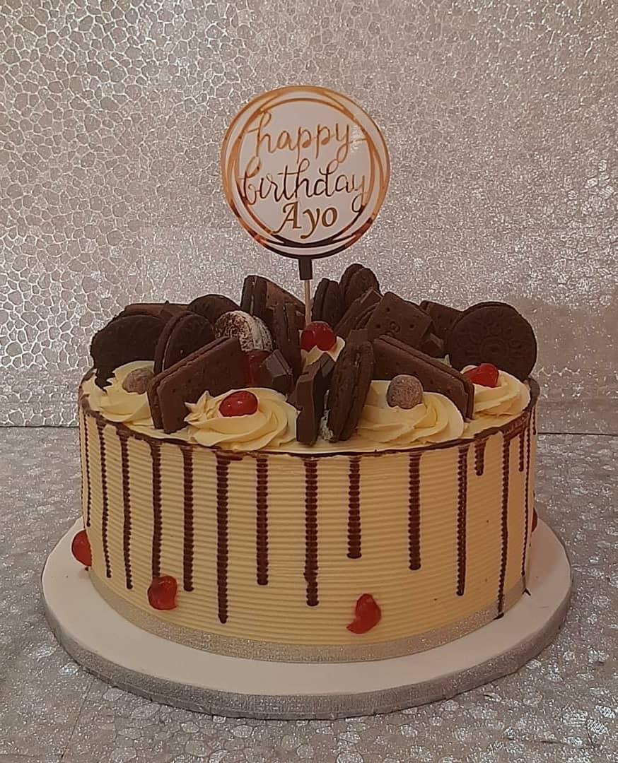 Round cake with dark drip icing, chocolate decorations, and a celebration topper.