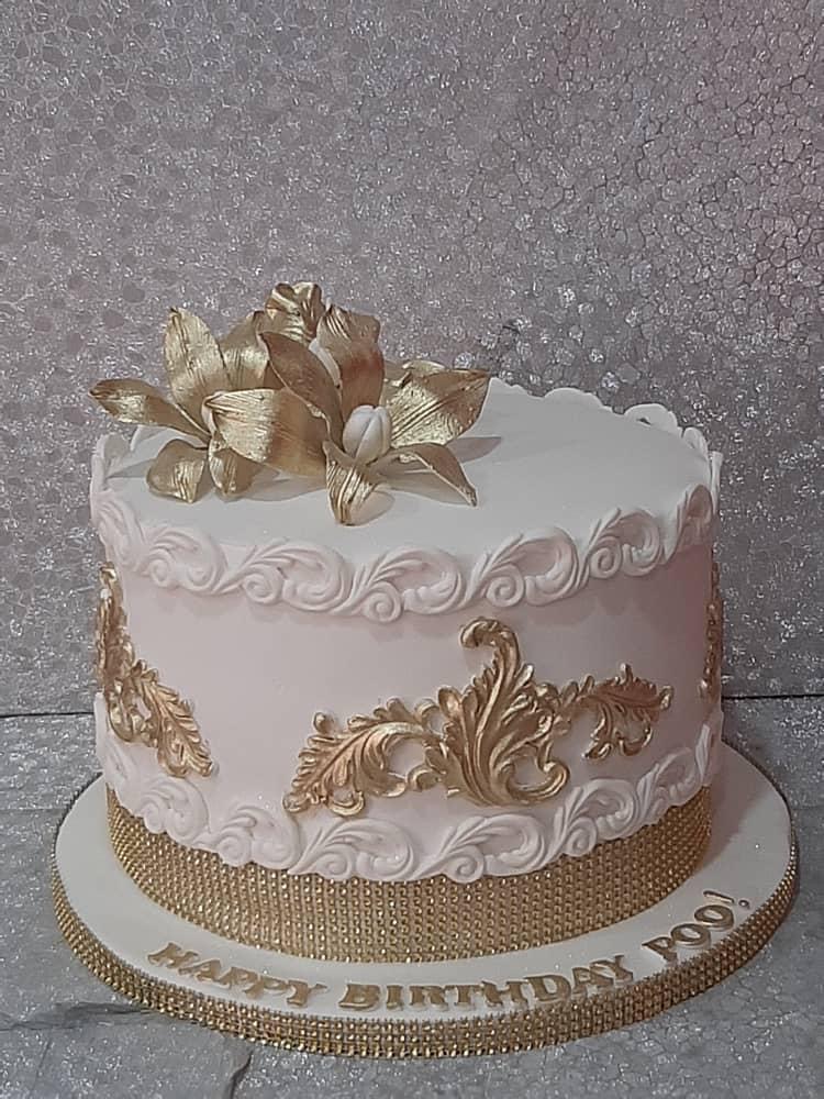 White cake with ornate gold piping and a gold bow on top.
