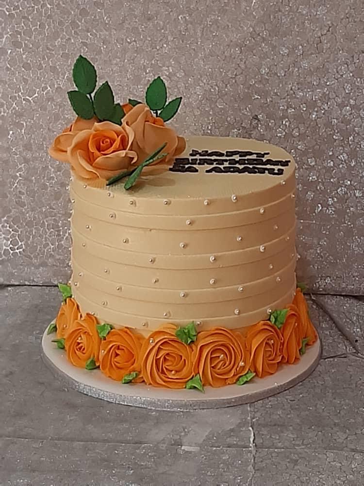 Pale round cake with horizontal ridges and orange roses around the base.