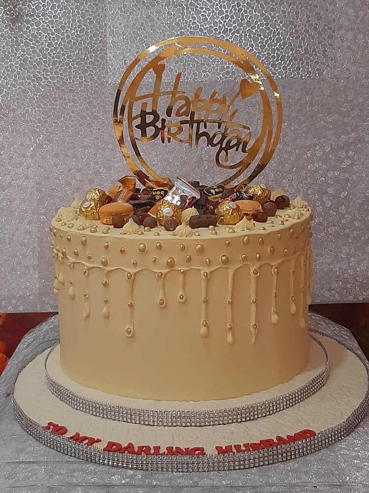 Caramel-colored cake with drip icing, chocolate toppings, and a celebration sign.