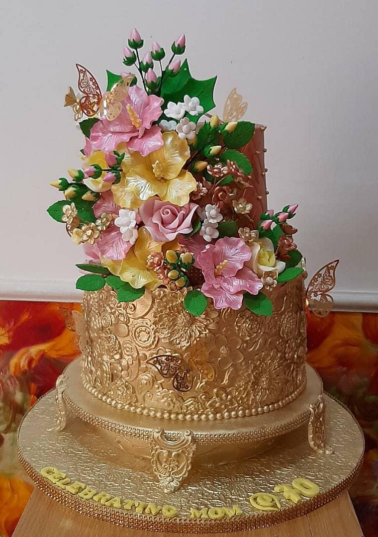 Gold-toned tiered cake decorated with a cascade of colorful flowers.