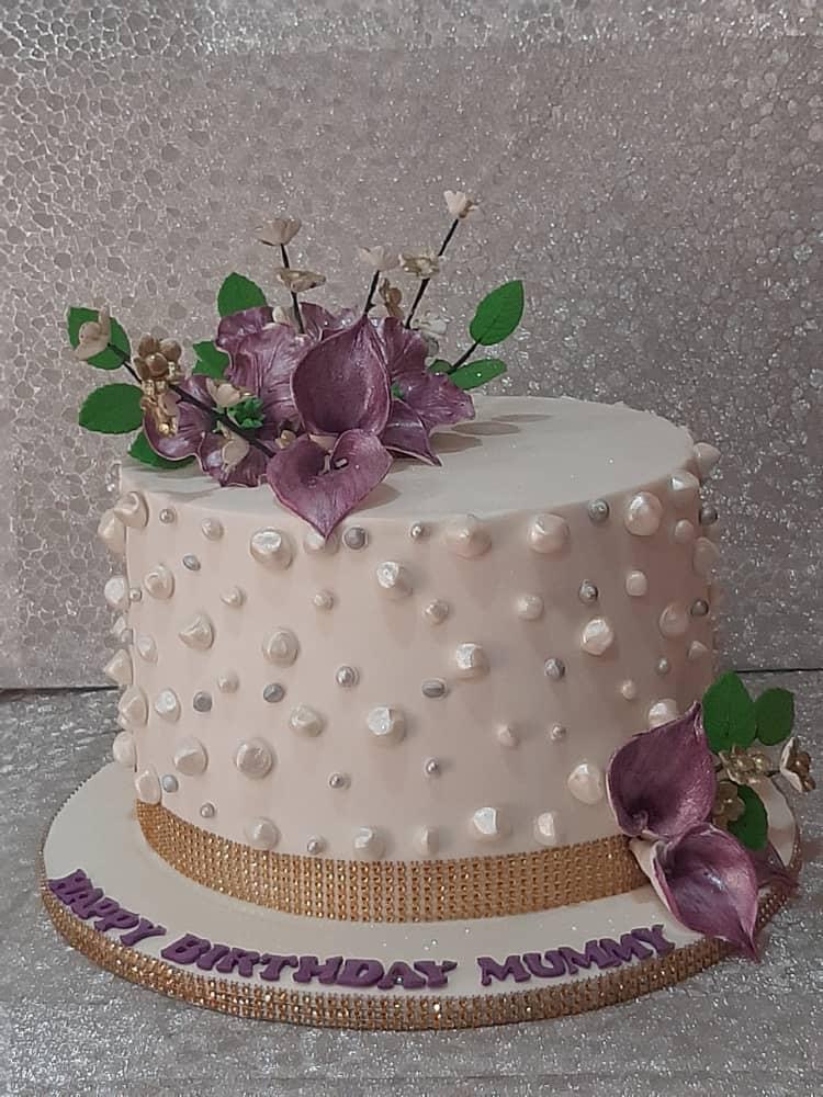 White cake covered with pearl-like decorations and topped with purple flowers.