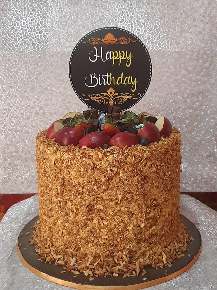 Round golden-crumb cake topped with fruit and a birthday sign.