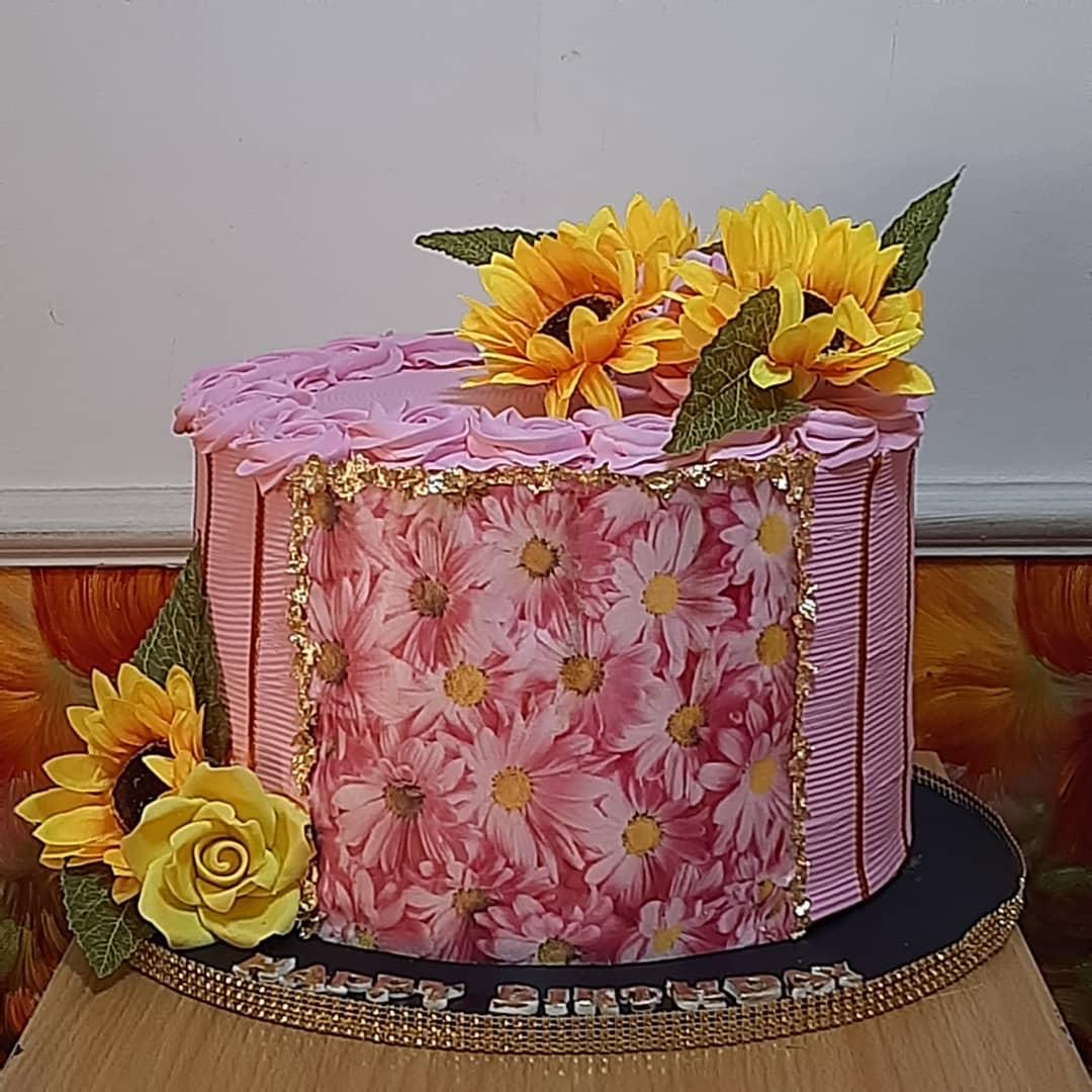 Pink square cake with floral icing and yellow sunflowers.