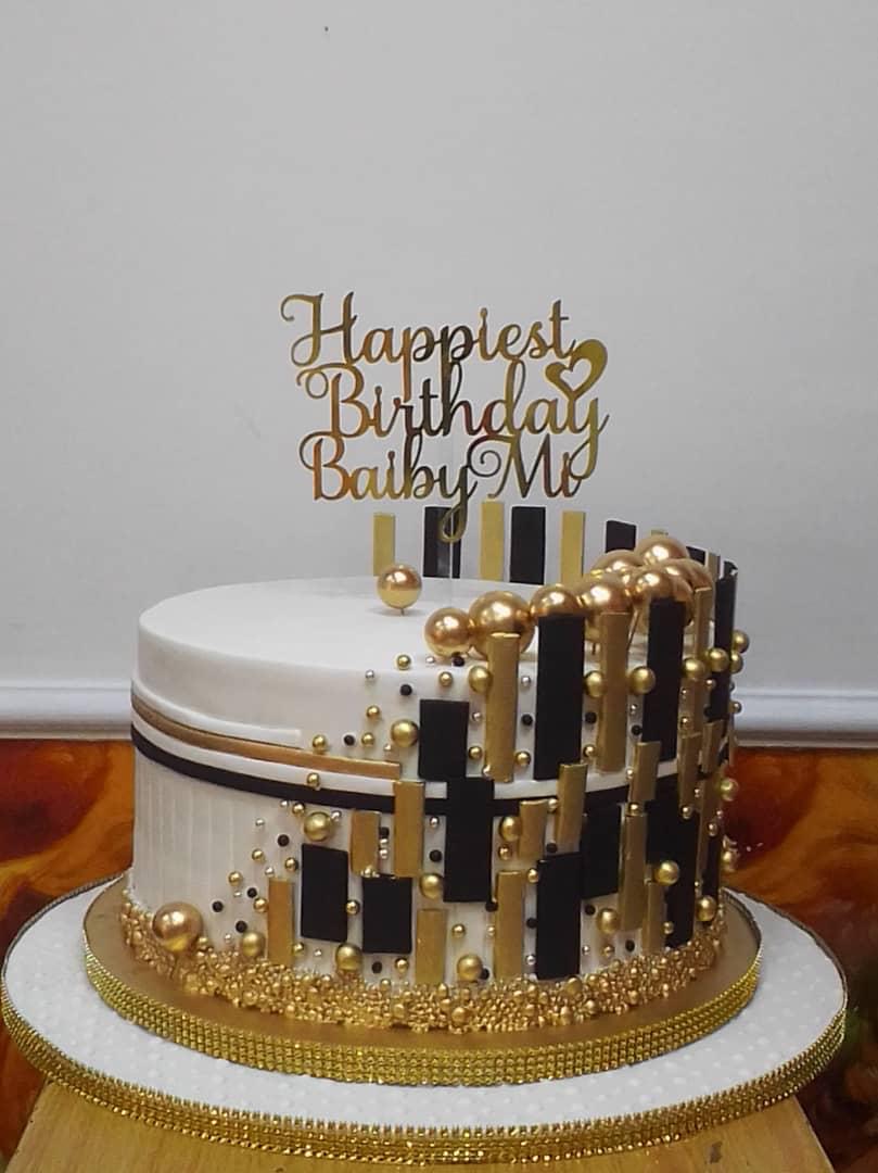Black-and-gold geometric celebration cake with tall lettering and decorative toppers.