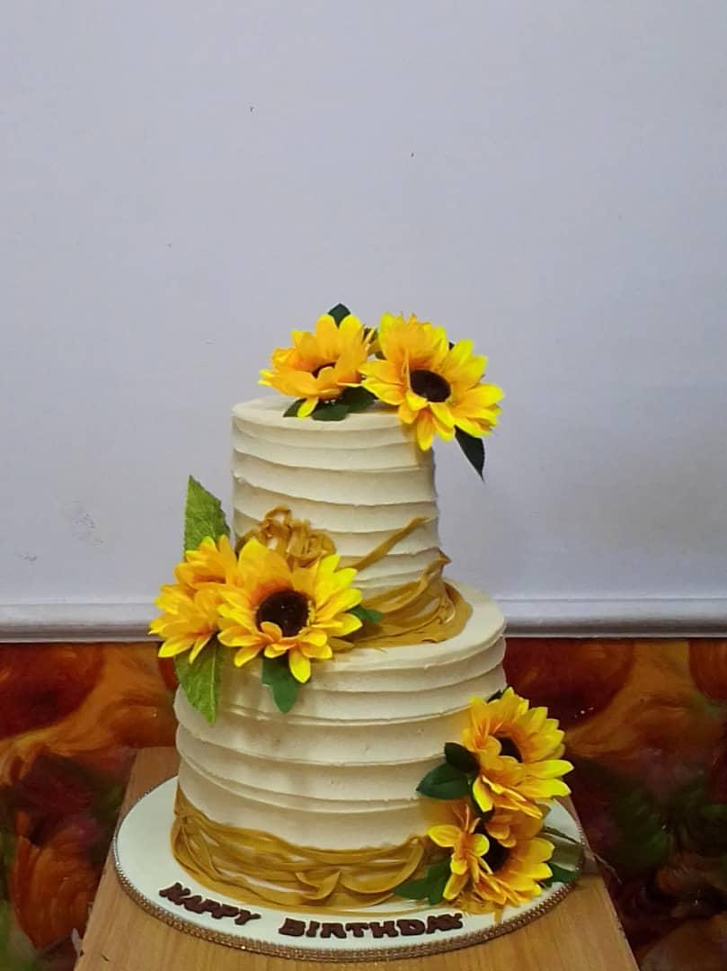 White tiered cake topped with yellow sunflowers and green leaves.