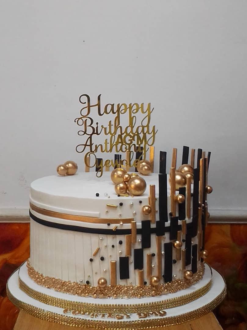 Black-and-gold celebration cake with tall lettering and toppers.