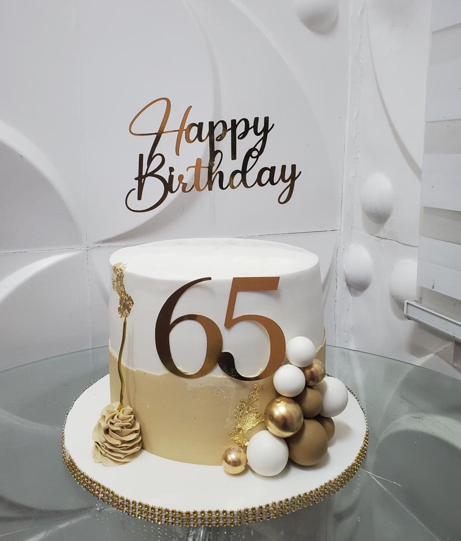 White and champagne-beige celebration cake with gold accents and decorative spheres.