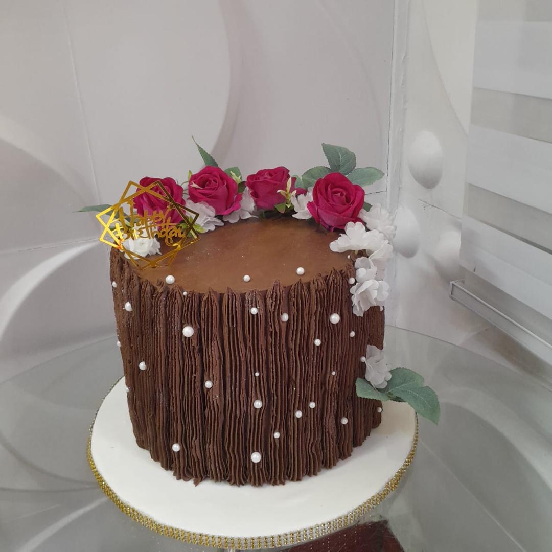 Chocolate cake decorated with pink roses, white flowers, and green leaves.