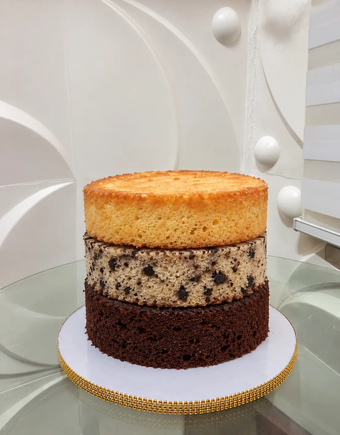 Three cake layers stacked: vanilla on top, cookies and cream with cookie pieces in the middle, and chocolate on the bottom.