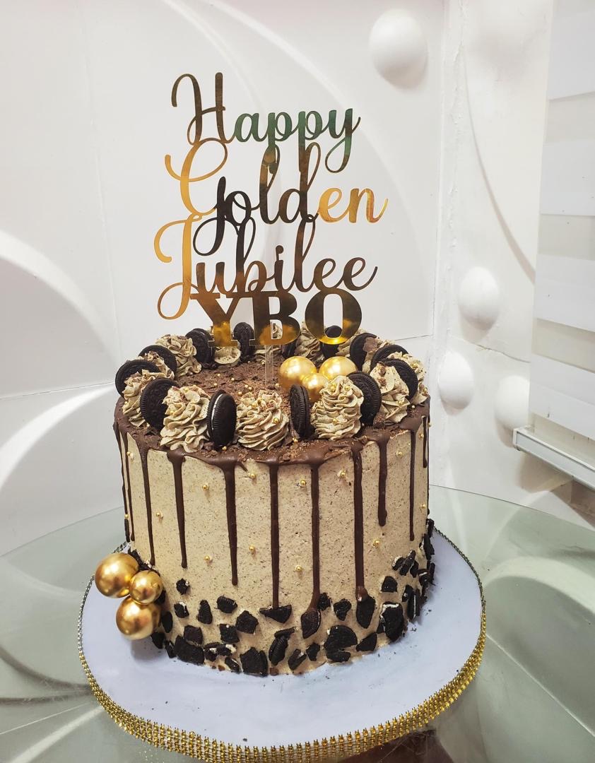 Tall chocolate drip cake with gold decorations and a Happy Golden Jubilee topper