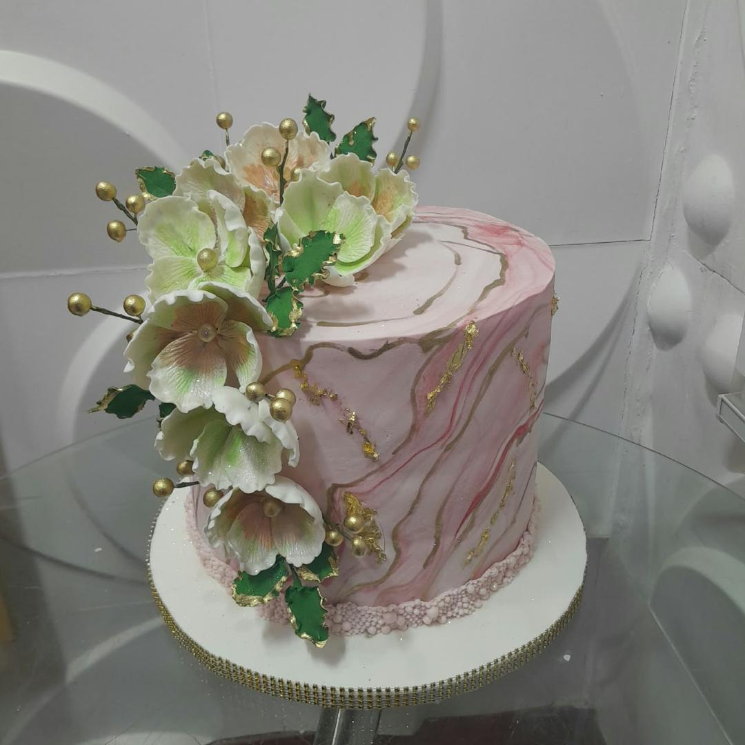 Pale pink cake with marbled frosting and a white floral arrangement.