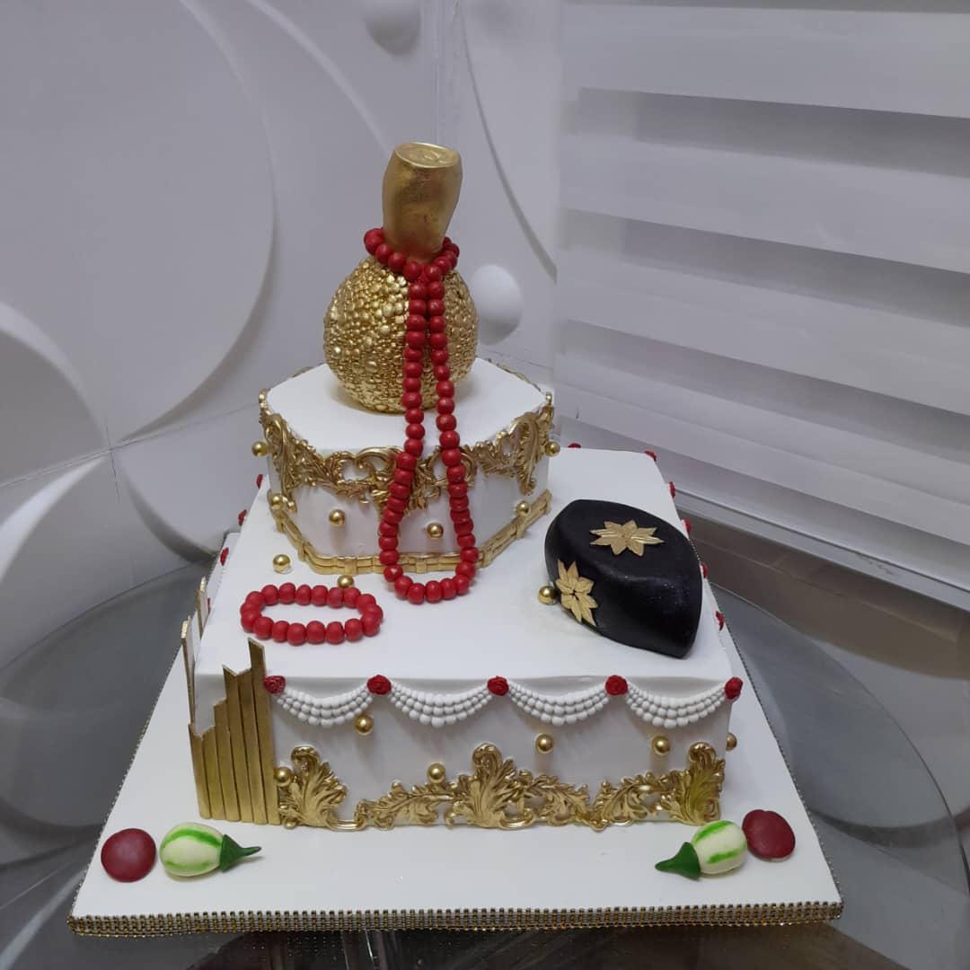 Square white celebration cake with red-and-gold details and decorative toppers.