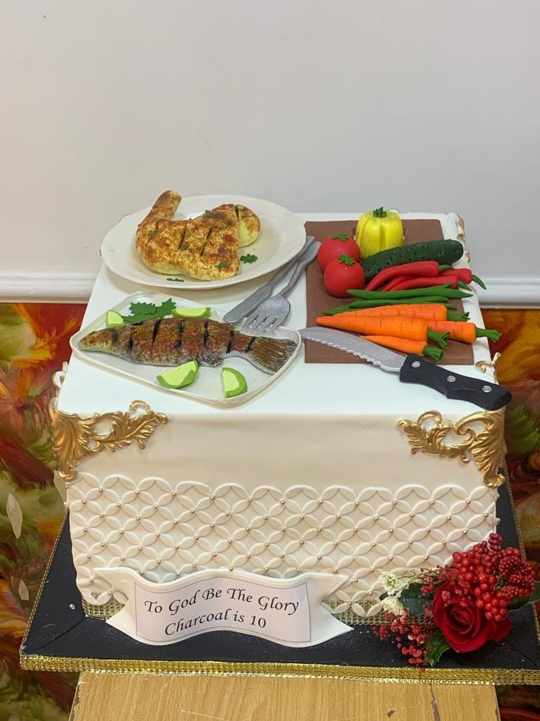 Rectangular celebration cake with textured white frosting, flowers, and decorative food toppers.