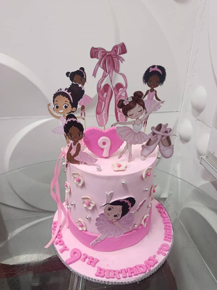 Pink celebration cake decorated with doll figures and a pink bow topper.
