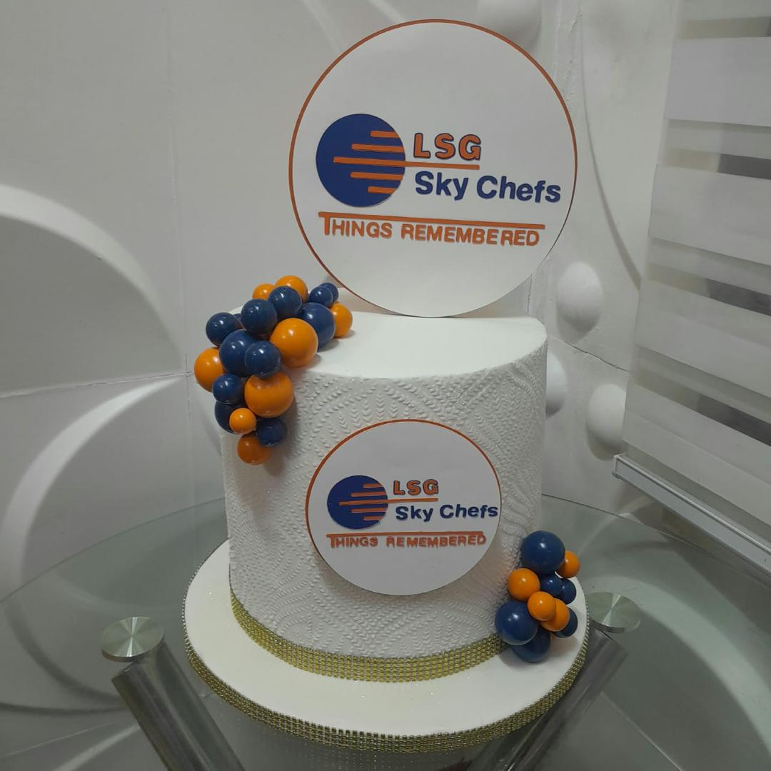 White corporate celebration cake with blue and orange logos.