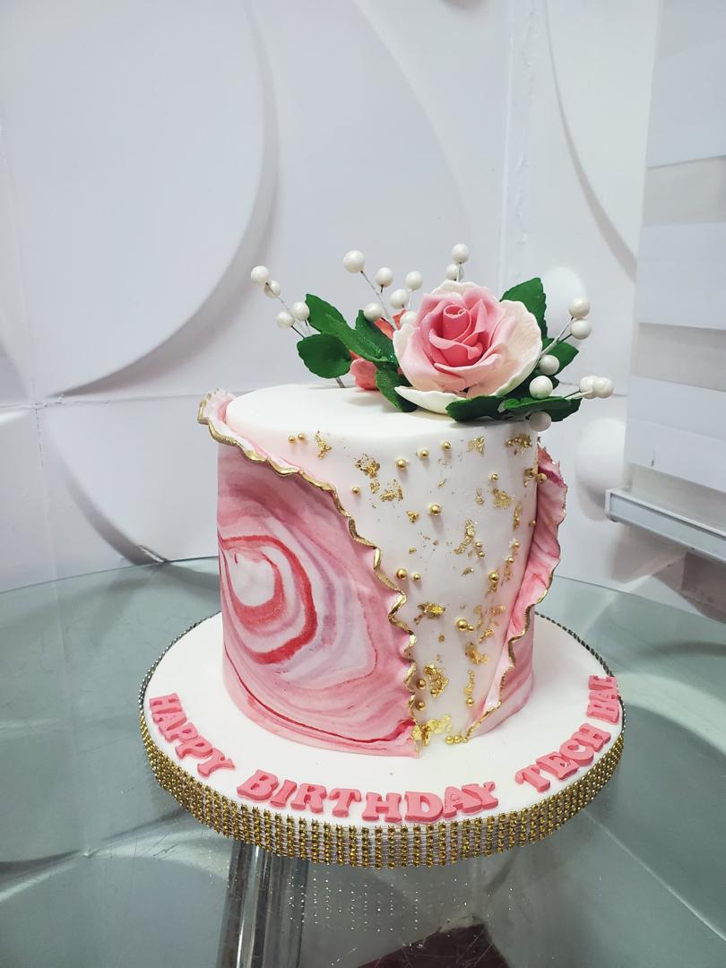 Pink-and-white celebration cake with flowers and a birthday plaque.
