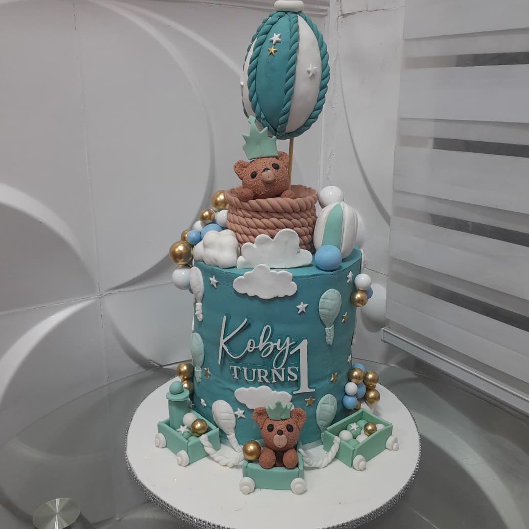 Teal celebration cake with teddy bears, clouds, and a hot-air-balloon topper.