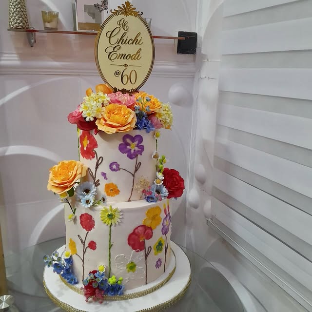 Two-tier white birthday cake with painted flowers and a gold 60 plaque